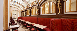 Elegantes Caf mit gewlbter, glserner Decke, roten Polsterbnken und klassischer Inneneinrichtung mit goldenen Wandverzierungen.
